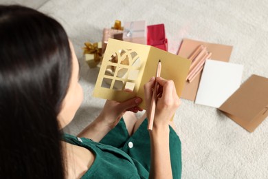 Woman writing message in greeting card on floor in living room, closeup