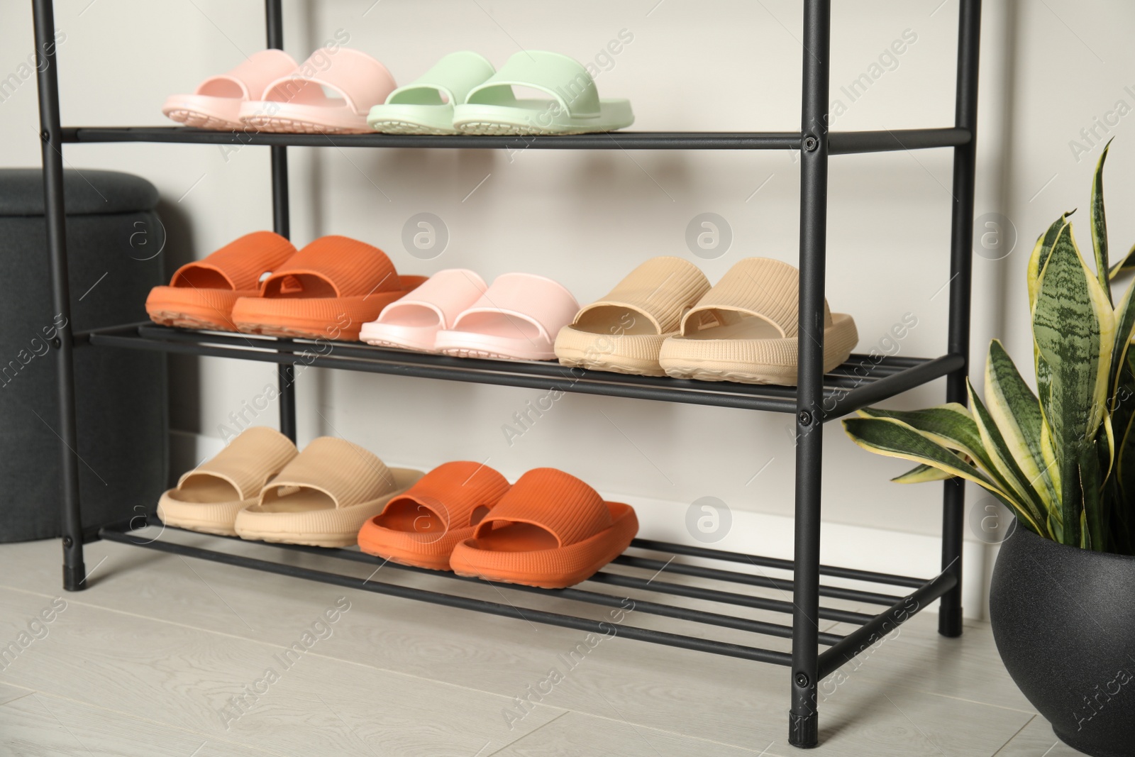 Photo of Shoe rack with different pairs of rubber slippers near white wall indoors