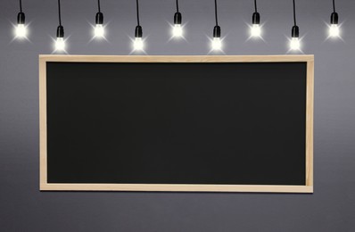 Glowing light bulbs and blackboard hanging on grey wall