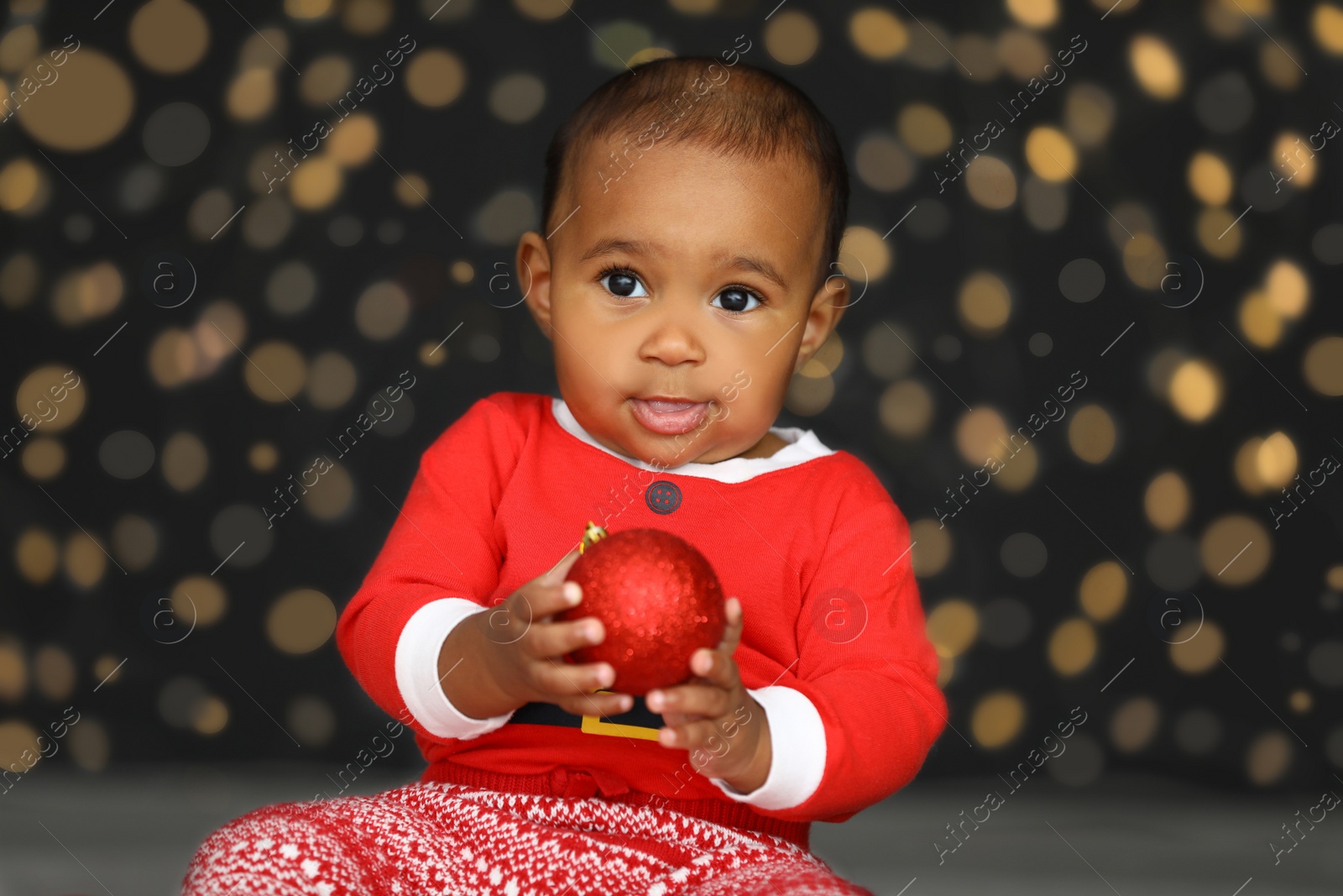 Image of Cute little African American baby with Christmas ball and blurred lights on dark background