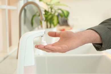 Photo of Man using automatic soap dispenser in kitchen, closeup