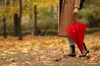 Photo of Woman with red umbrella walking in autumn park, closeup. Space for text