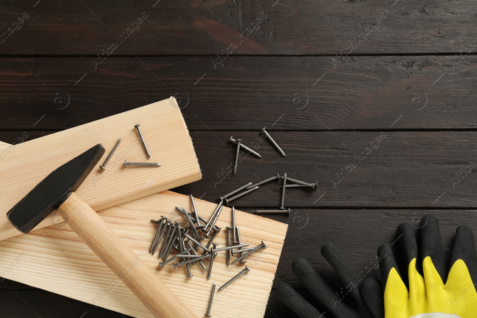 Photo of Hammer, planks, gloves and metal nails on wooden table, flat lay. Space for text