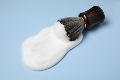 Photo of Brush with shaving foam on light blue background