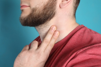 Young man checking pulse on neck against color background, closeup