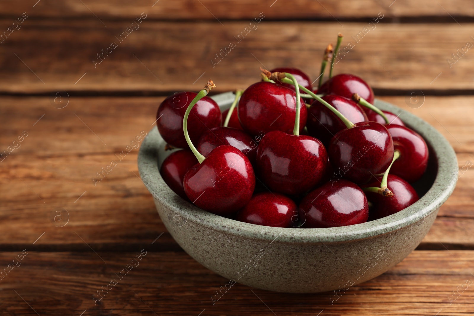 Photo of Bowl with ripe sweet cherries on wooden table, closeup