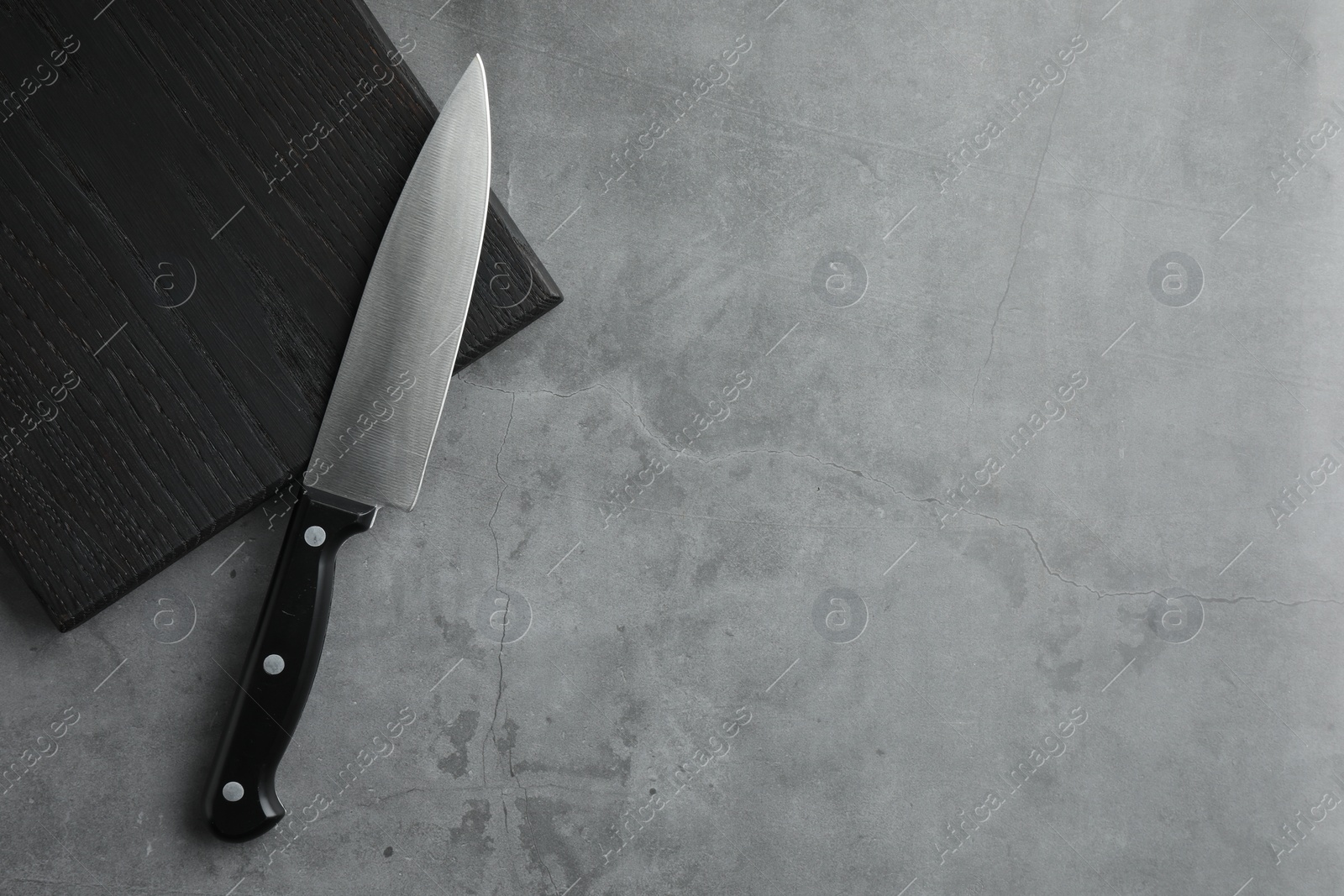 Photo of Knife and black wooden board on grey textured table, top view. Space for text