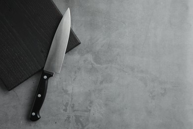 Photo of Knife and black wooden board on grey textured table, top view. Space for text