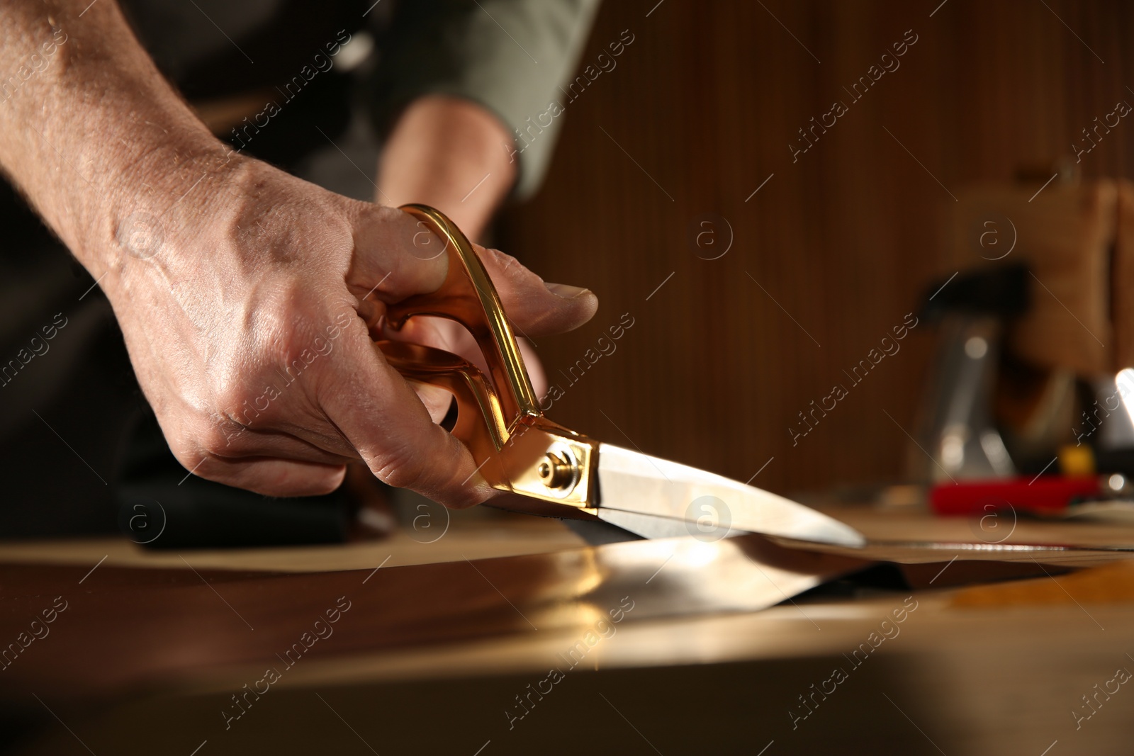 Photo of Man cutting leather with scissors in workshop, closeup