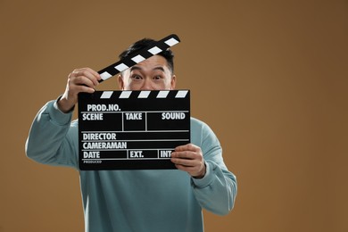 Photo of Emotional asian actor with clapperboard on brown background, space for text. Film industry