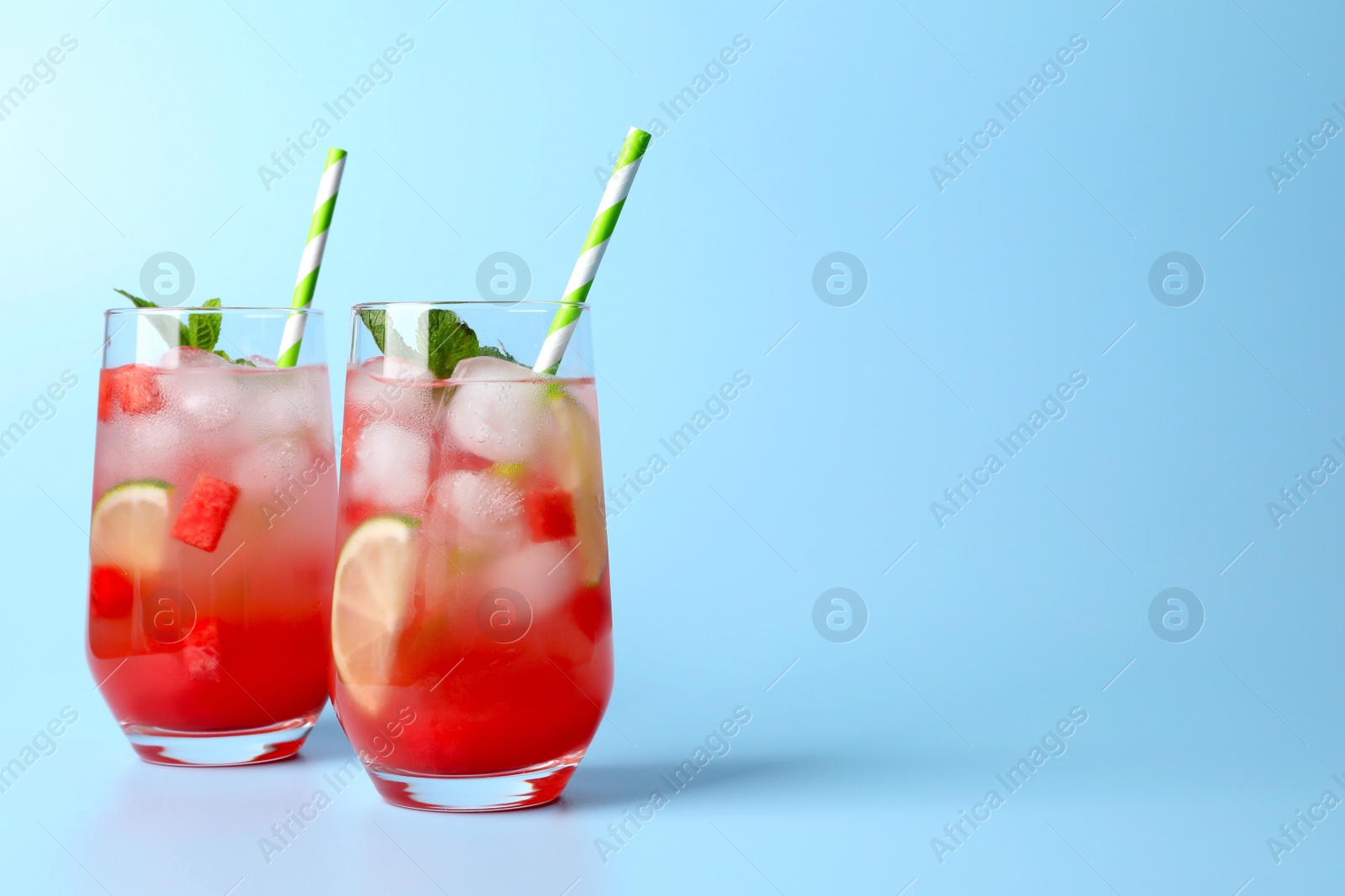 Photo of Tasty summer watermelon drink with lime in glasses on pale light blue background. Space for text