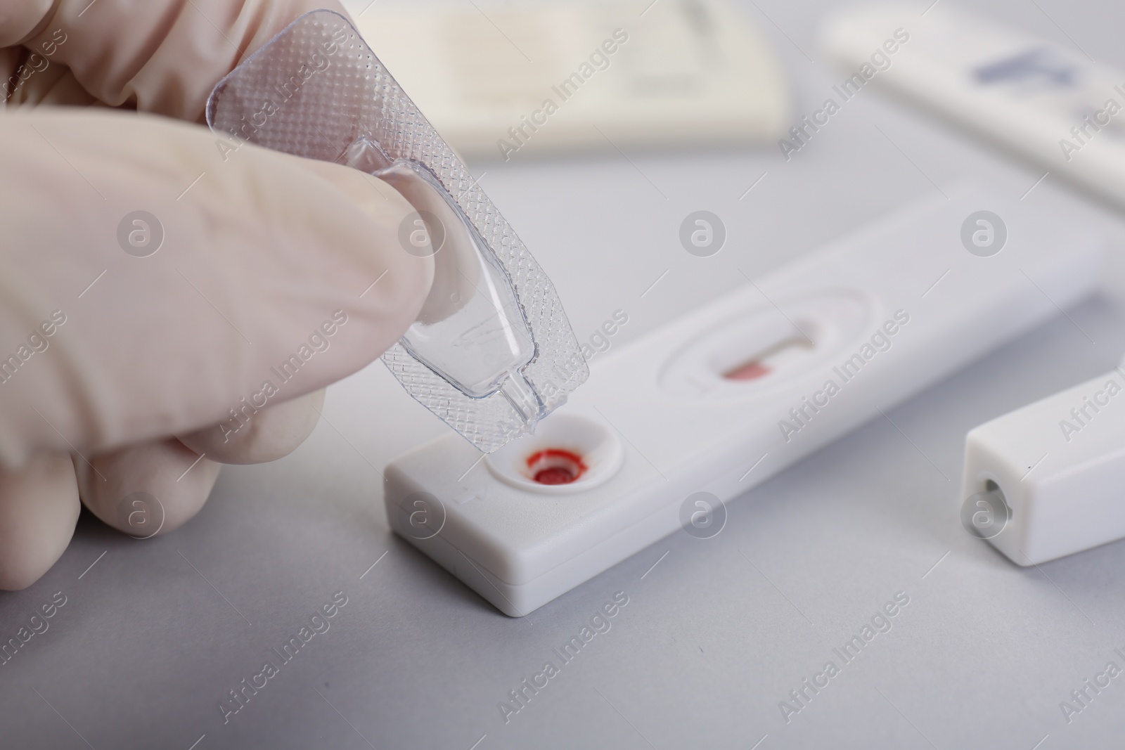 Photo of Doctor dropping buffer solution onto disposable express test cassette on light background, closeup