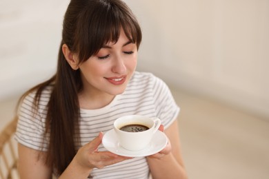 Smiling woman drinking coffee at breakfast on blurred background. Space for text