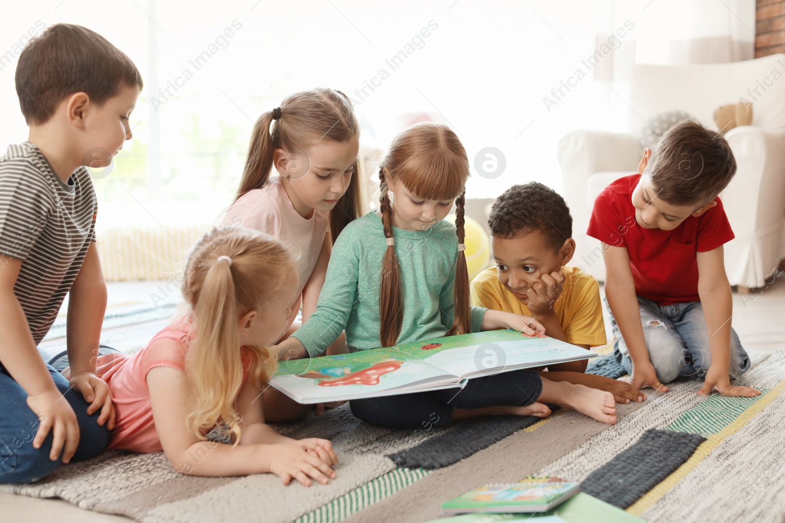 Photo of Cute little children reading book together indoors. Learning by playing