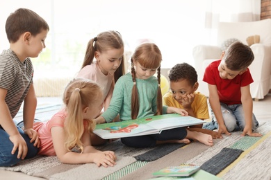 Photo of Cute little children reading book together indoors. Learning by playing