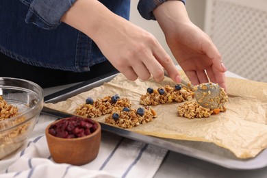 Making granola bars. Woman putting mixture of oat flakes, dry fruits and other ingredients onto baking tray at table in kitchen, closeup