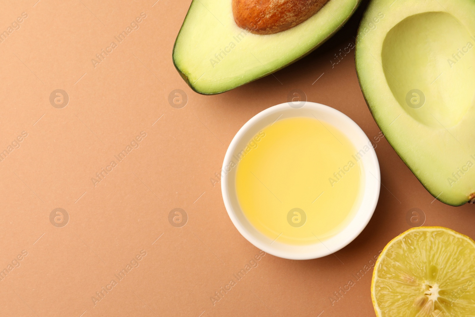 Photo of Cooking oil in bowl, fresh avocados and lemon slice on beige background, flat lay. Space for text