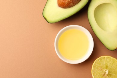 Cooking oil in bowl, fresh avocados and lemon slice on beige background, flat lay. Space for text