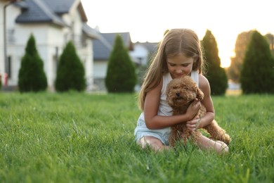 Photo of Beautiful girl with cute Maltipoo dog on green lawn in backyard