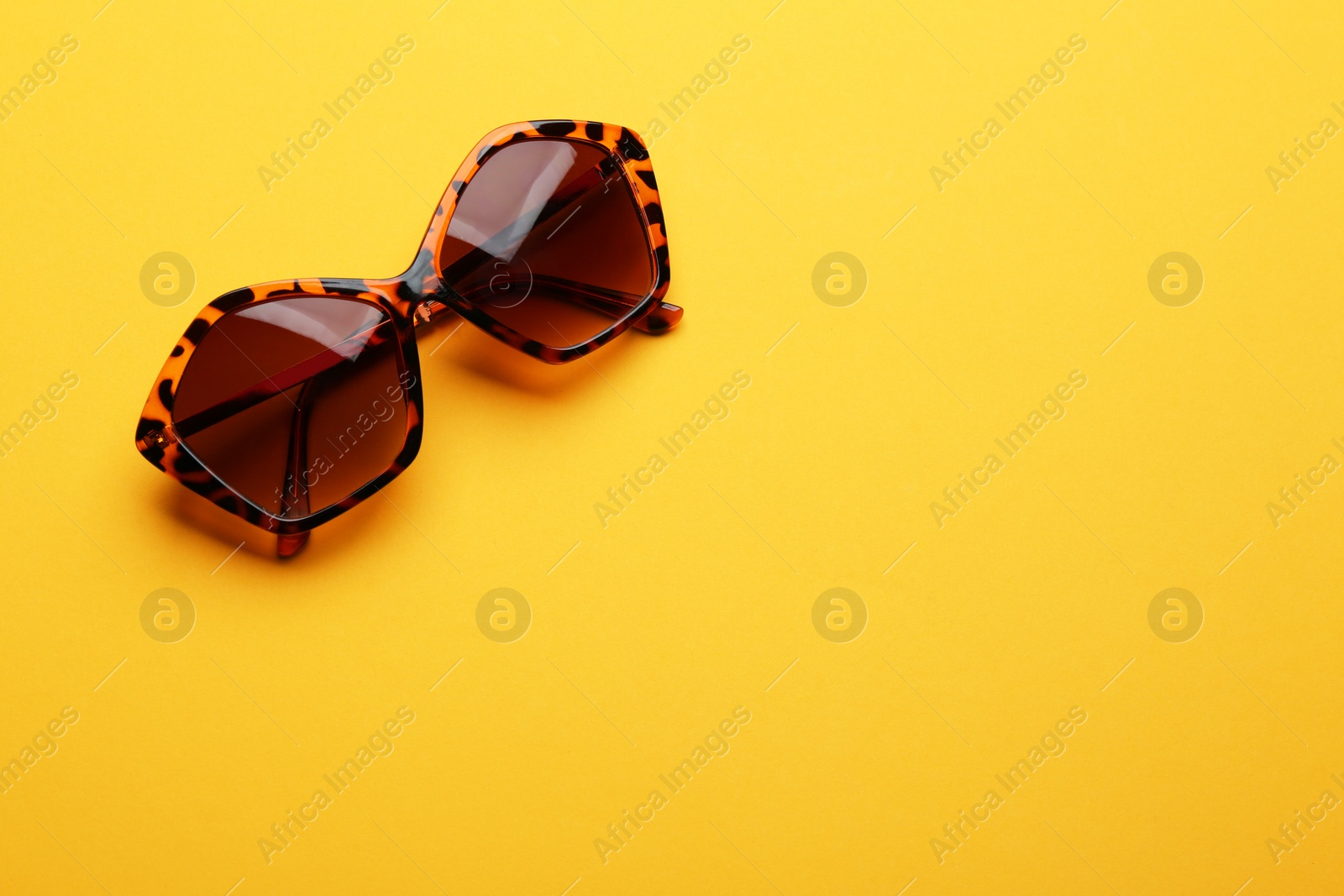 Photo of Stylish sunglasses on yellow background, space for text. Fashionable accessory