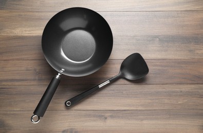Photo of Black metal wok and spatula on wooden table, top view