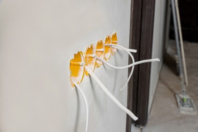 Photo of Holes for socket in white wall with cables indoors. Installation of electrical wiring