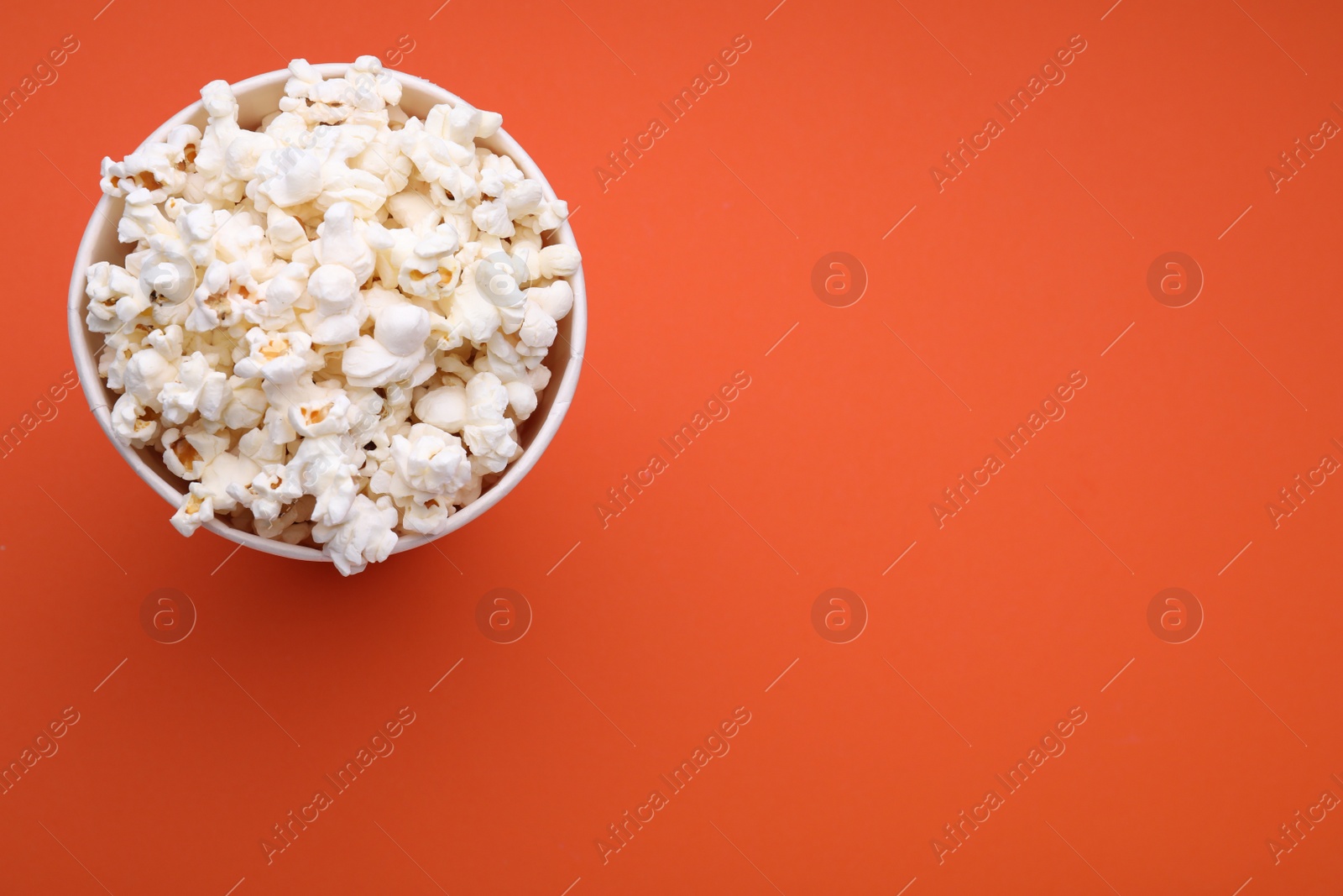 Photo of Bucket of tasty popcorn on orange background, top view. Space for text
