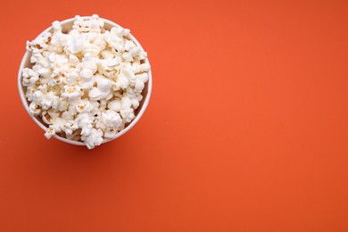 Bucket of tasty popcorn on orange background, top view. Space for text