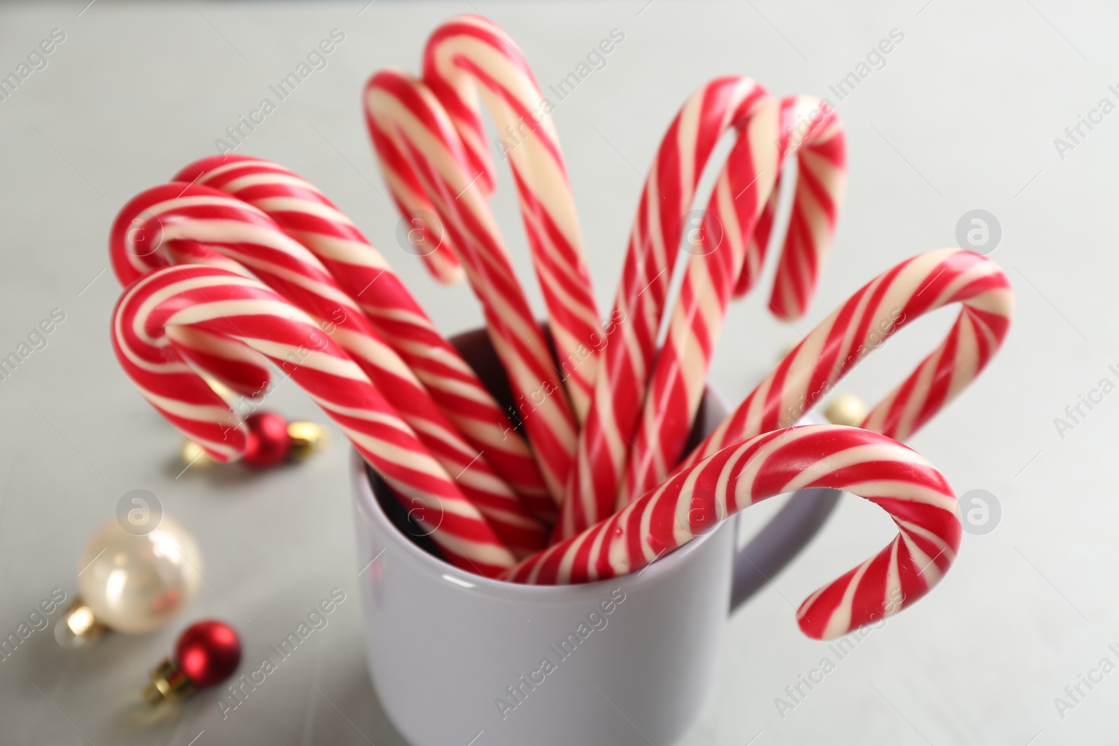 Photo of Christmas candy canes in cup on light grey table, closeup
