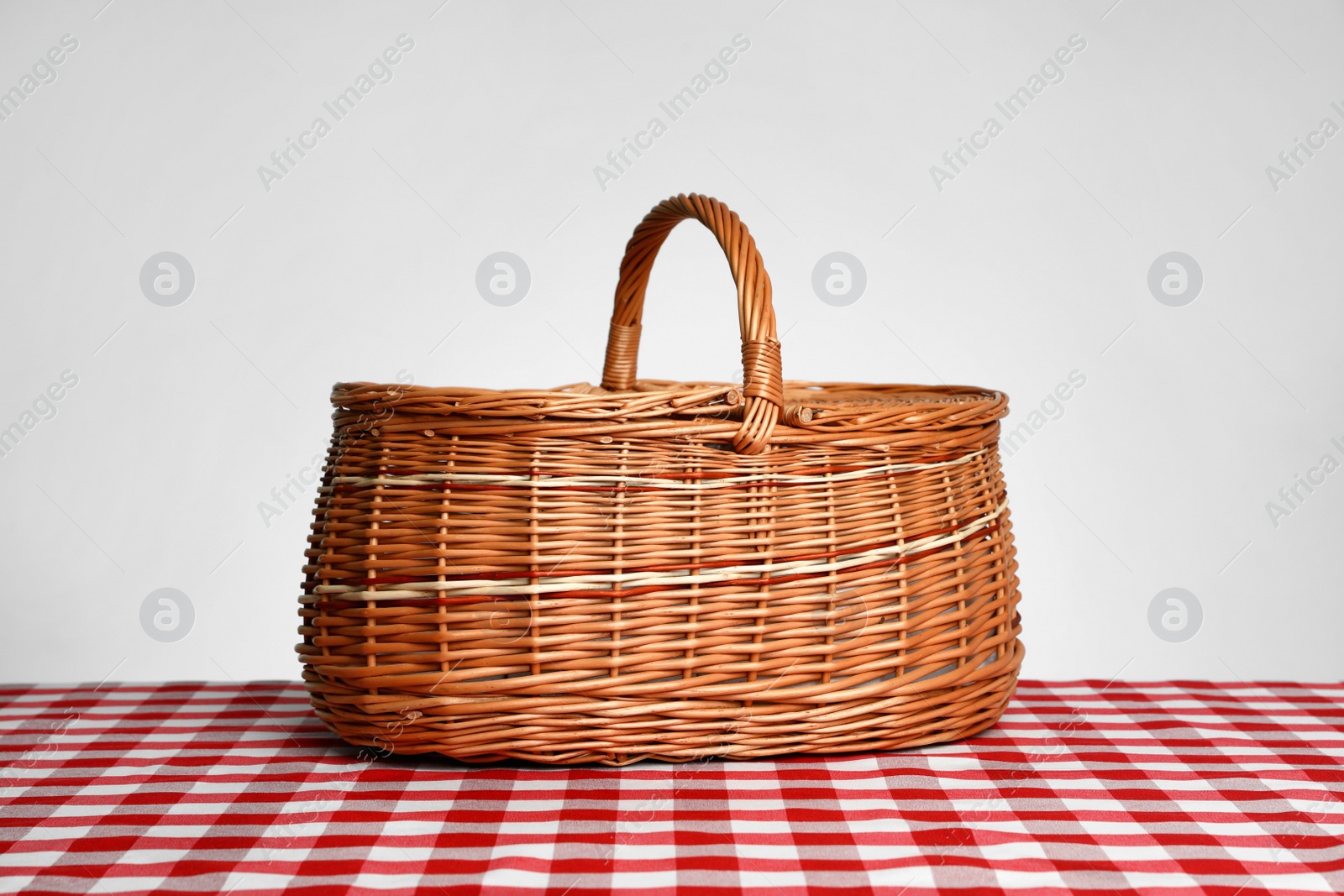 Photo of Closed wicker picnic basket on checkered tablecloth against white background