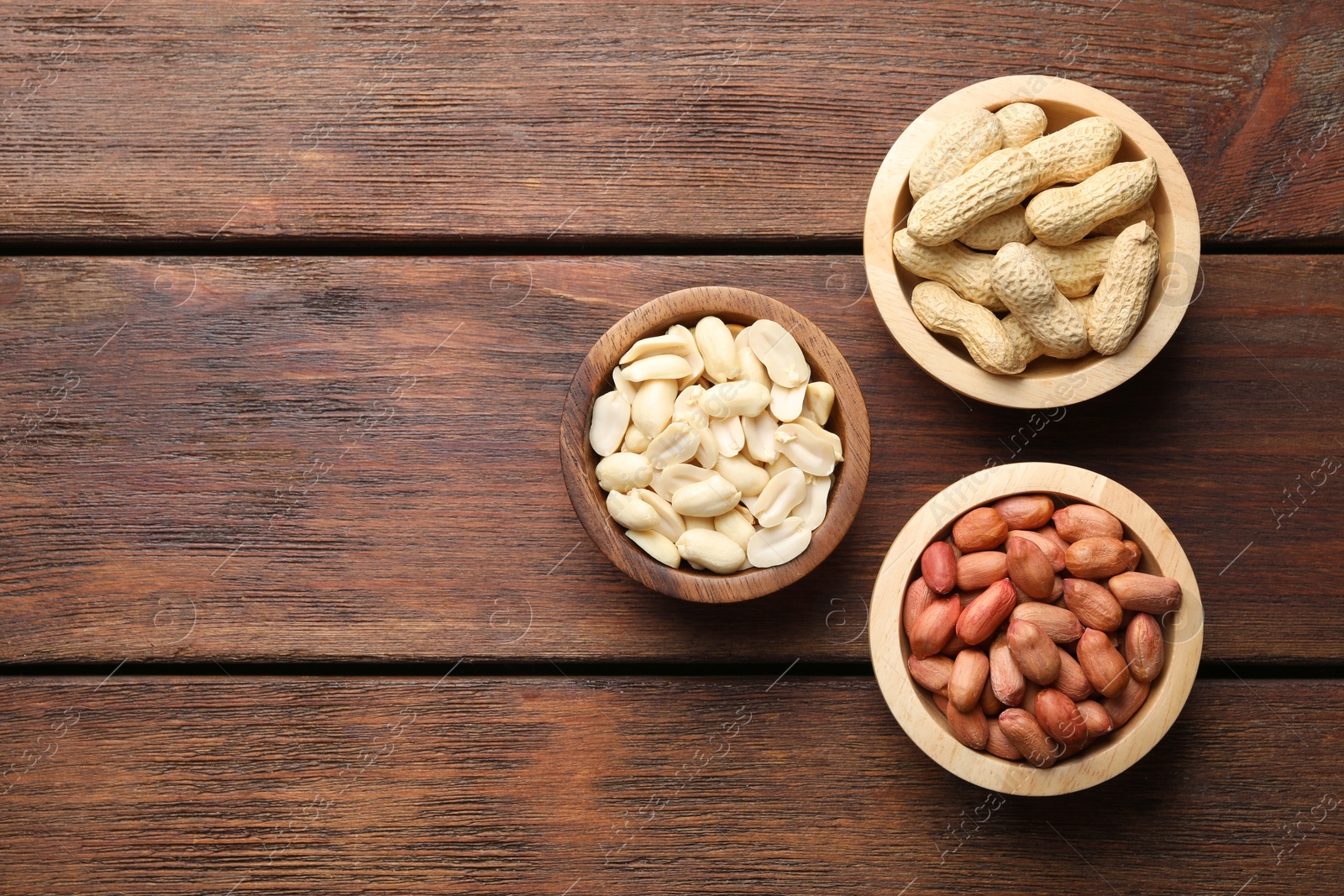 Photo of Fresh peanuts in bowls on wooden table, top view. Space for text