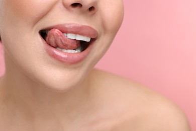 Photo of Woman with beautiful lips licking her teeth on pink background, closeup