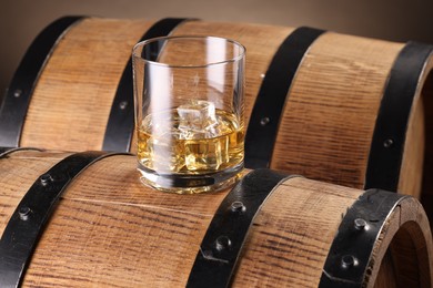 Photo of Whiskey with ice cubes in glass on wooden barrel, closeup