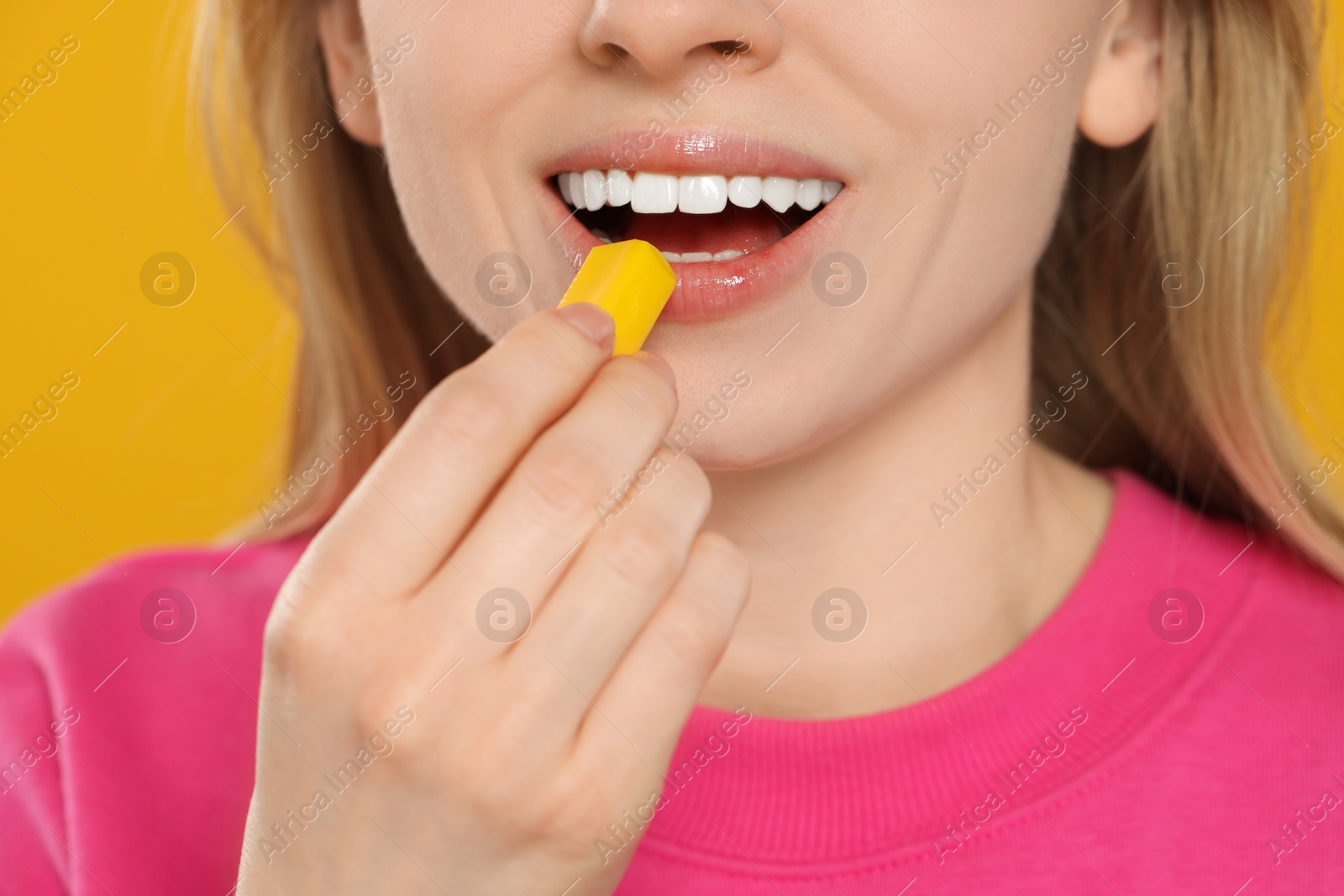Photo of Woman putting bubble gum into mouth on yellow background, closeup