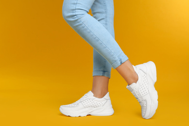 Photo of Woman wearing stylish sneakers on yellow background, closeup