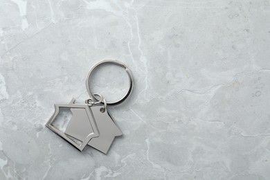 Photo of Metal keychain in shape of houses on grey marble table, top view. Space for text