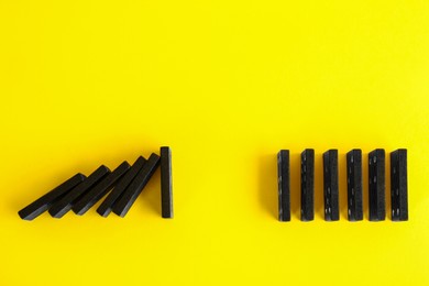Photo of Black domino tiles on yellow background, flat lay. Space for text