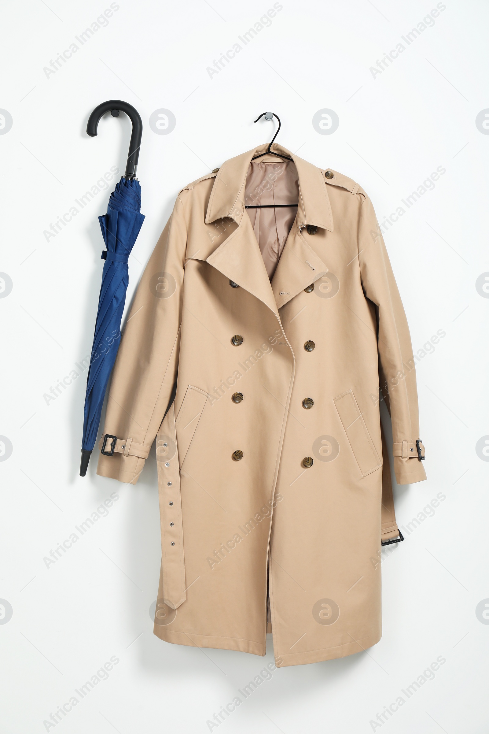 Photo of Hanger with beige trench coat and blue umbrella on white wall