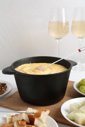 Photo of Fondue pot with tasty melted cheese, forks, wine and different snacks on table