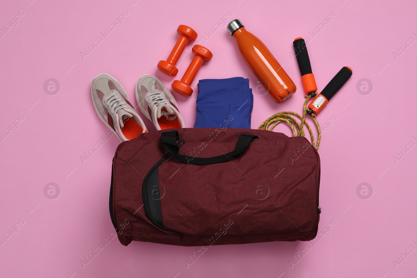 Photo of Gym bag and sports equipment on light pink background, flat lay