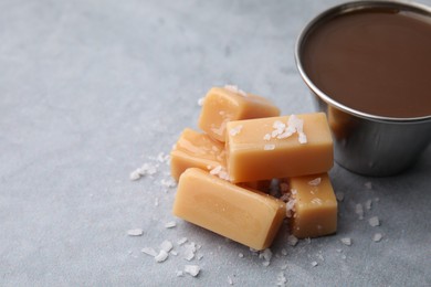 Yummy caramel candies, sauce and sea salt on grey table, closeup. Space for text