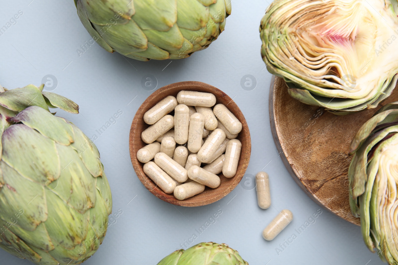 Photo of Bowl with pills and fresh artichokes on light grey background, flat lay