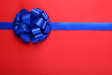 Photo of Blue ribbon with bow on red background, top view. Space for text