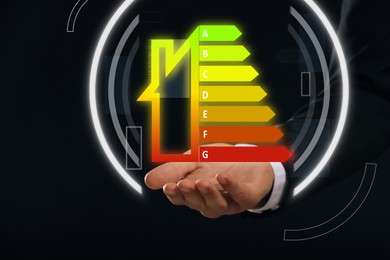 Energy efficiency. Man holding virtual colorful rating against black background, closeup