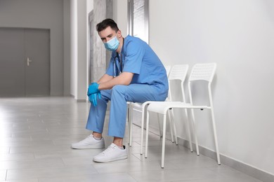 Photo of Exhausted doctor sitting on chair in hospital hallway