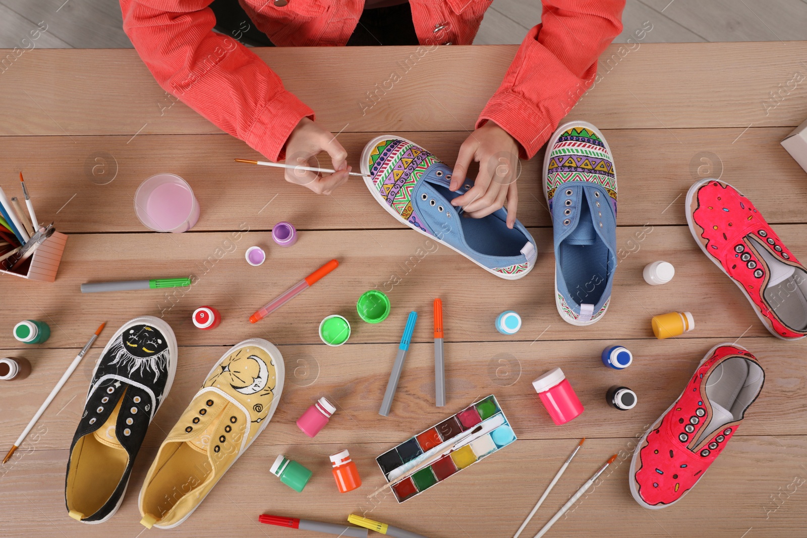 Photo of Woman painting on sneaker at wooden table, top view. Customized shoes