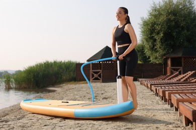 Woman pumping up SUP board on river shore