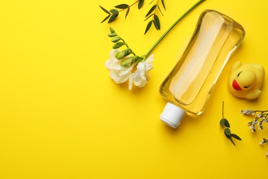 Bottle of baby oil, leaves and flowers on yellow background, flat lay. Space for text