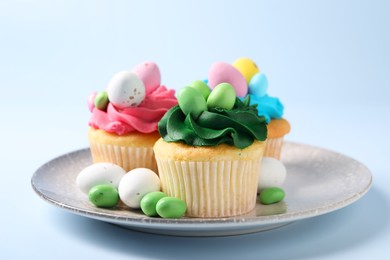 Photo of Tasty cupcakes with Easter decor on light blue background, closeup