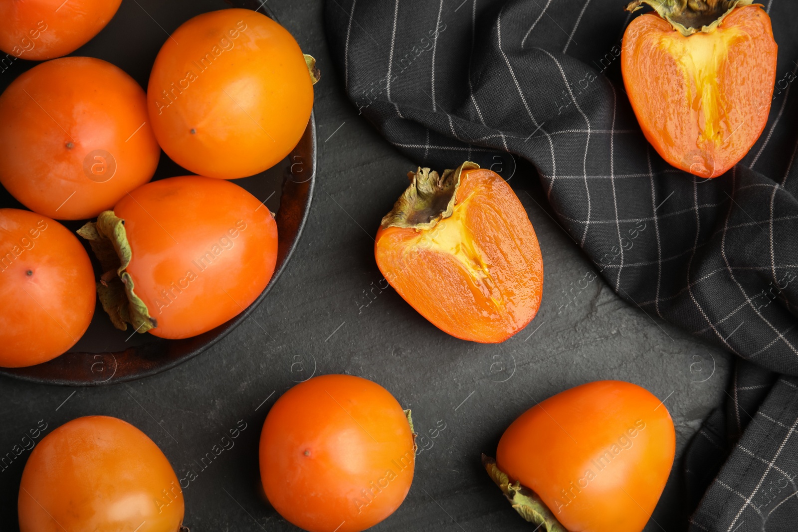 Photo of Tasty ripe persimmons on black slate table, flat lay